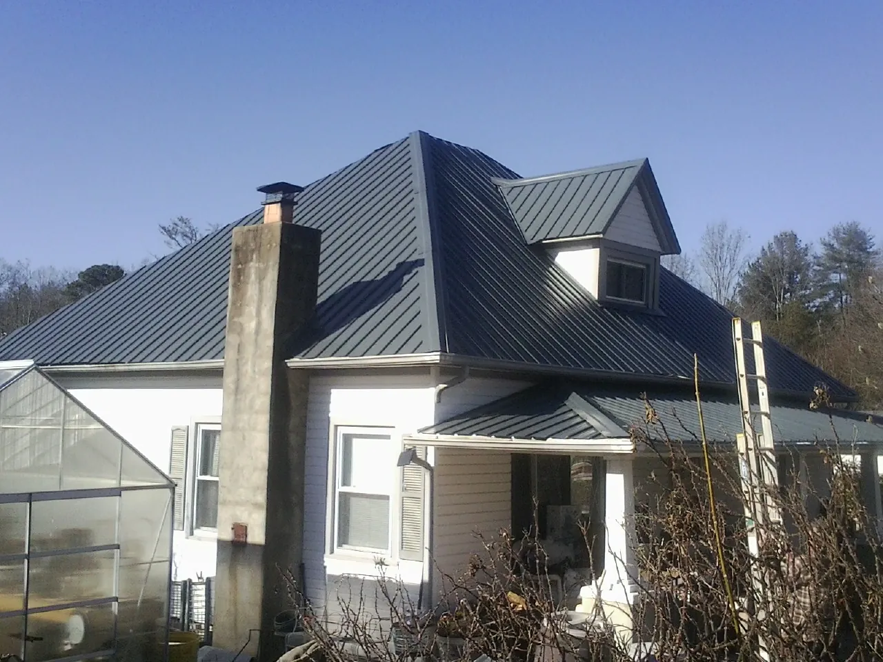 Dark blue standing seam metal roof on a white farmhouse with dormer — Slate & Tile Roof Repair by Roofing Brothers in Ebensburg
