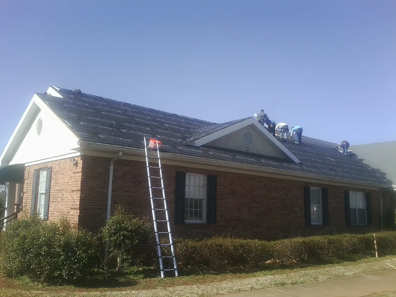 Crew tearing shingles off a brick ranch roof with a ladder set — Emergency Roof Repair work by our crew in Ebensburg