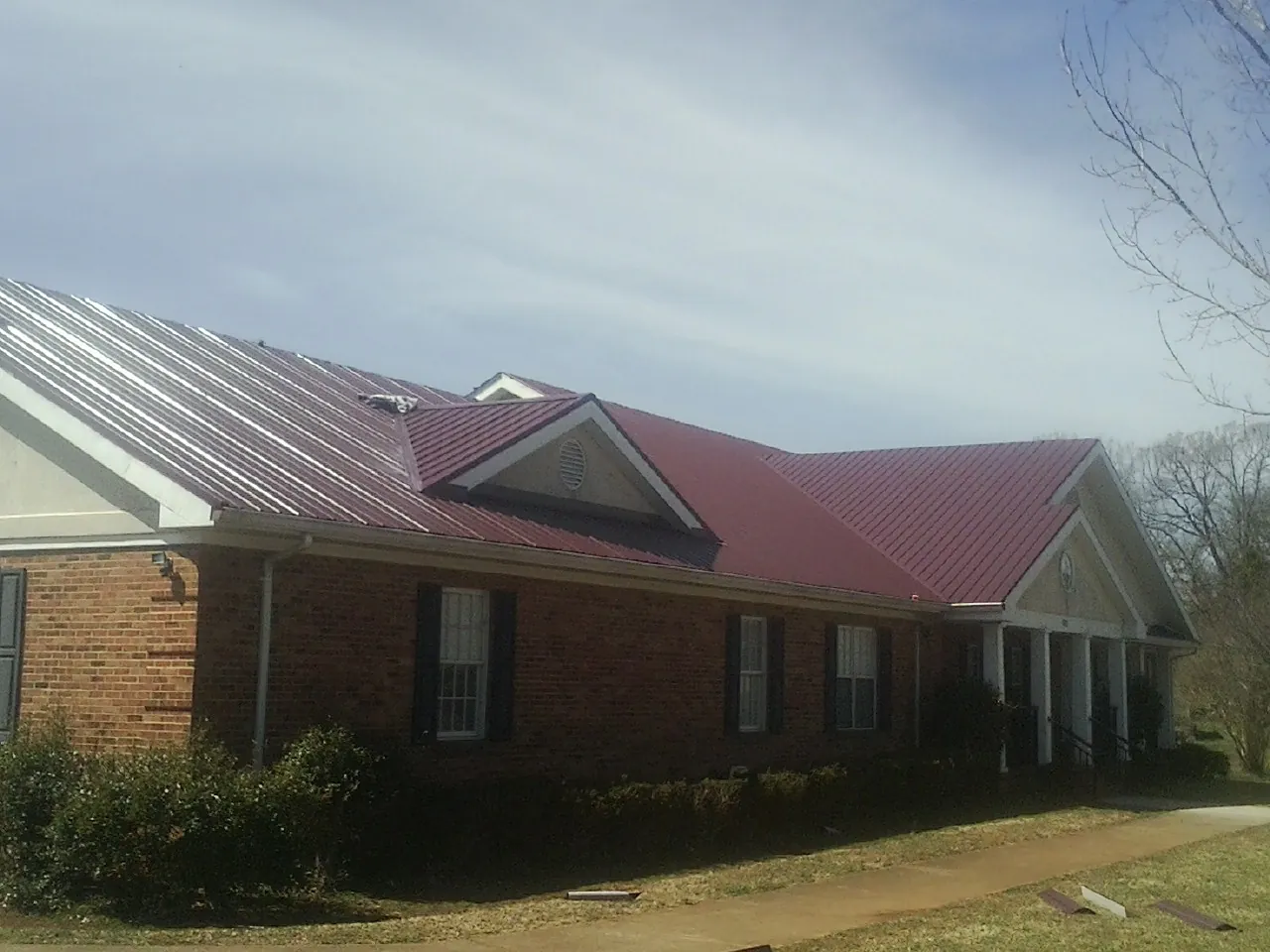 Red metal roof with gabled entries on a long brick building, from a Hail Damage Roof Repair job in Ebensburg