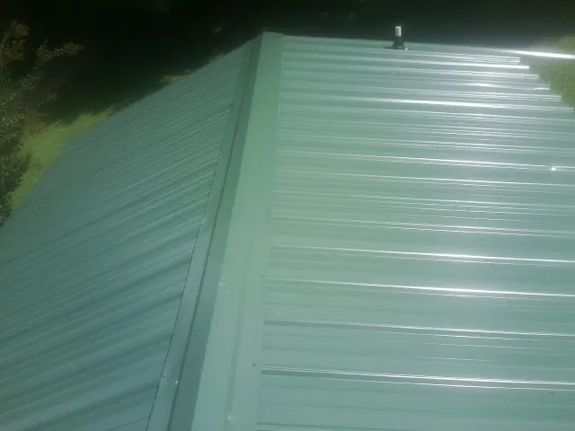 New green metal panels meeting at the ridge of a roof — Flat Roof Repair work by our crew in Ebensburg