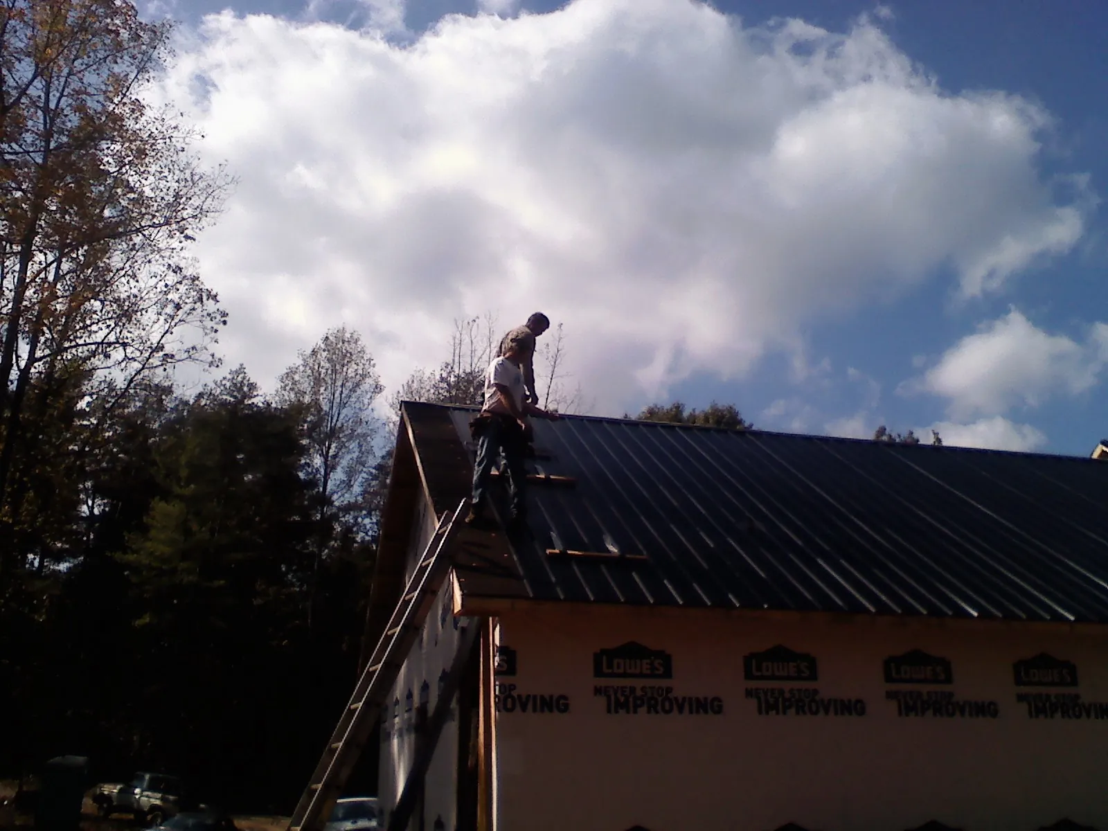 Roofer fastening dark metal panels high against a cloudy sky, from a Roof Inspection job in Ebensburg