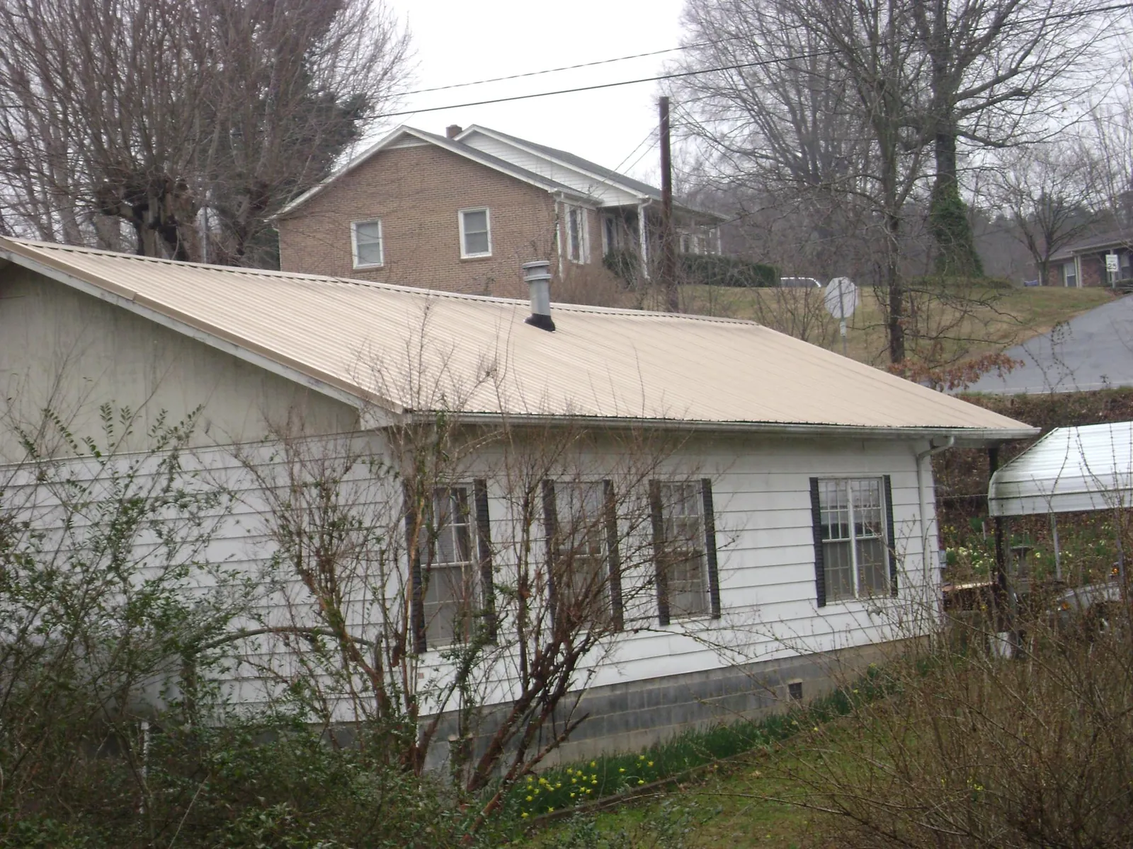 Tan metal roof on a white sided house set into a hillside — Commercial Roofing by Roofing Brothers in Ebensburg