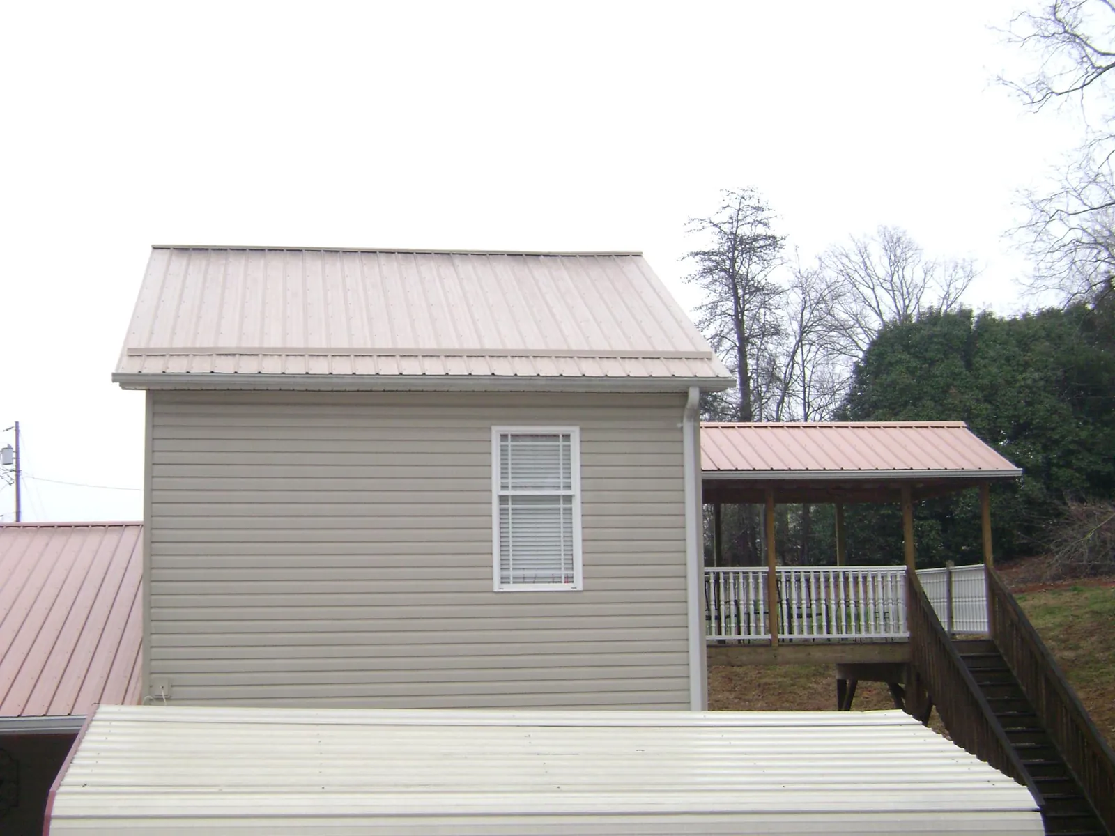 Tan metal roofs on a two story addition and attached porch, from a Roof Replacement job in Ebensburg